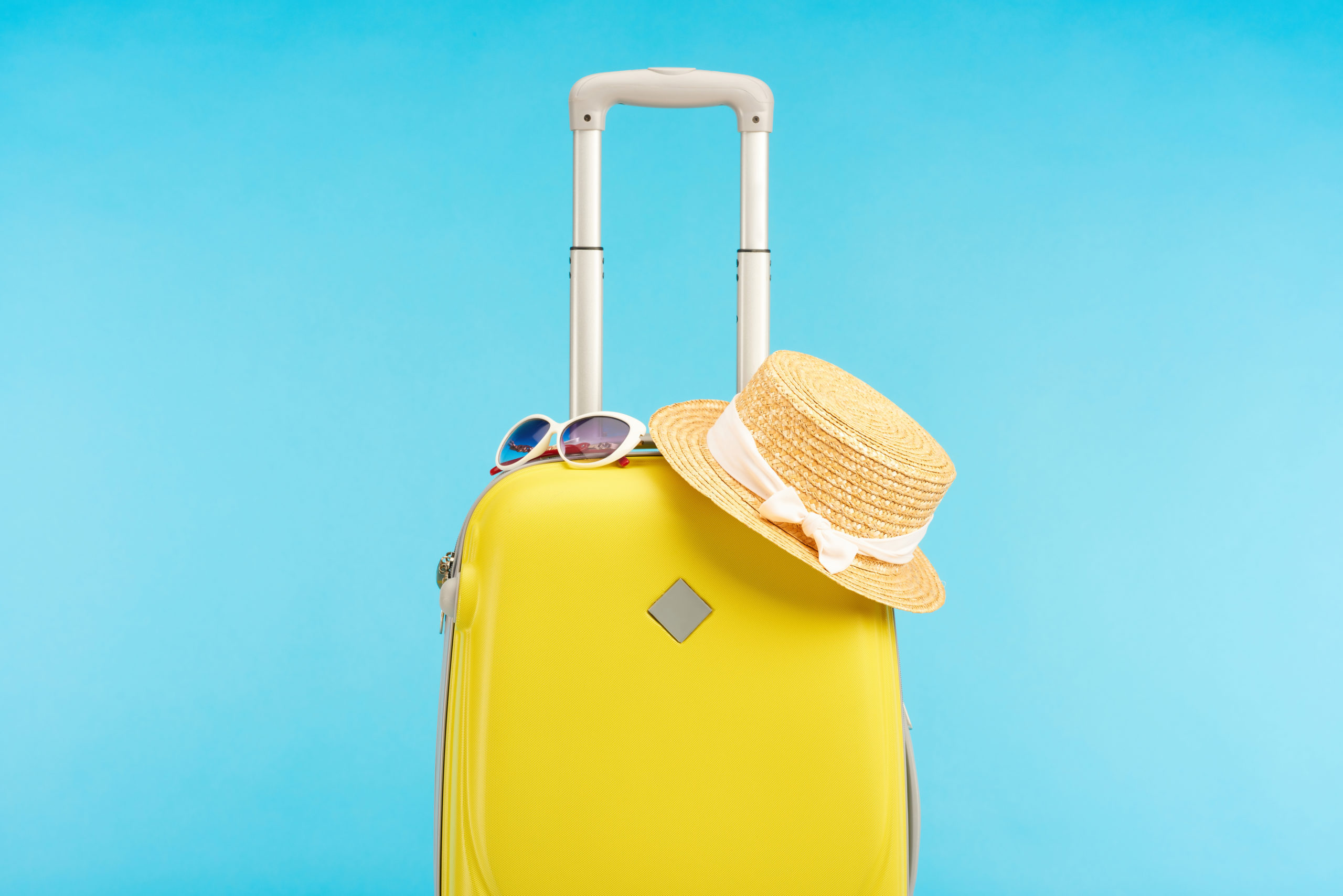 Yellow suitcase on blue background with hat and sunglasses on top