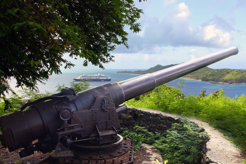 American WWII cannon in the foreground & beautiful landscape with a cruise ship in the background, Bora Bora, French Polynesia.