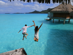 Happiness jump of young couple on the water. Over water bungalows at Bora Bora, French Polynesia.