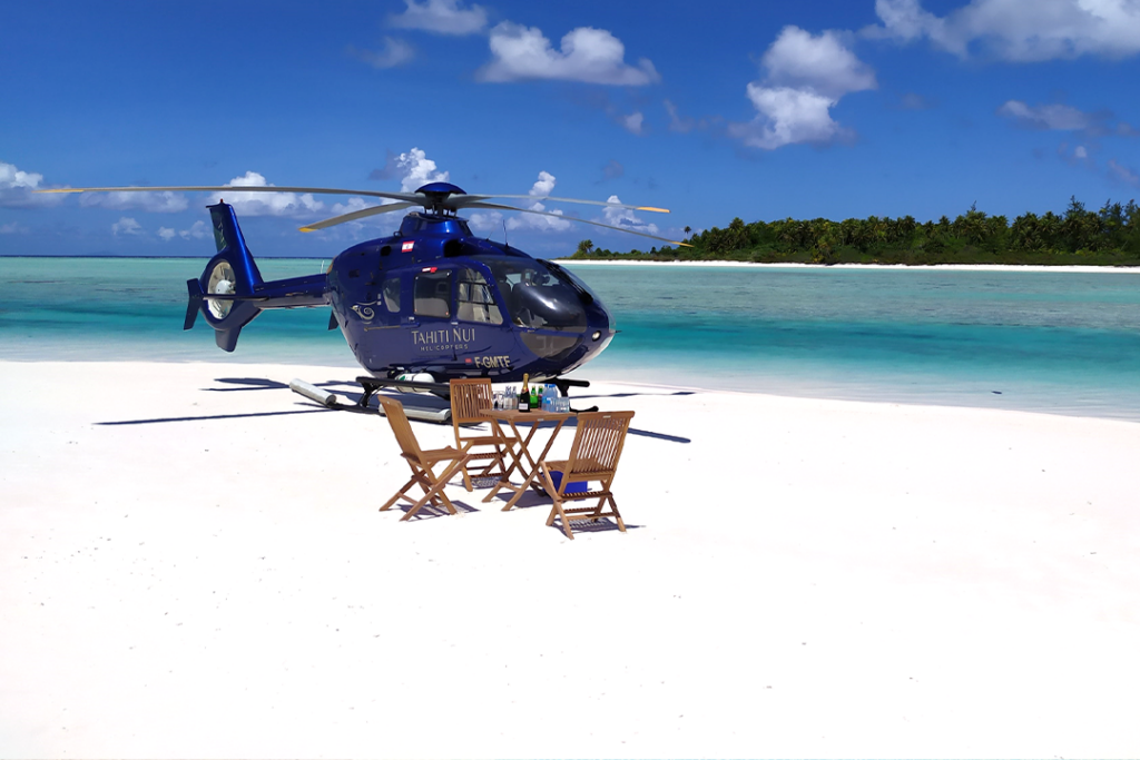 Tahiti Nui Helicopter on the white sand beach with a table and 3 chairs with the crystal blue water in the background