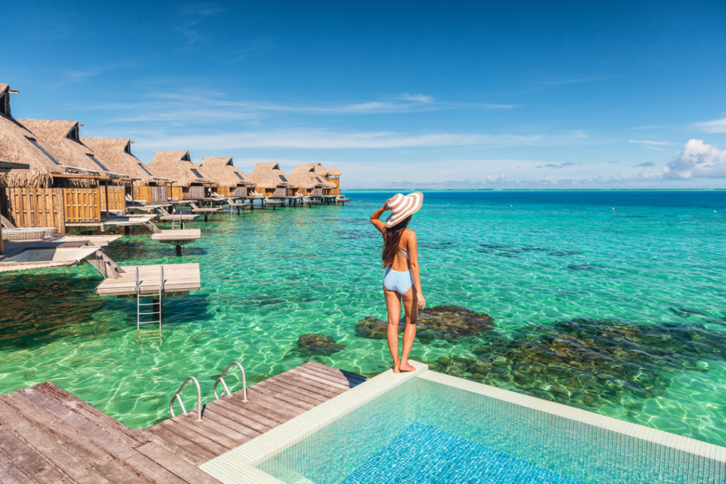 Travel luxury resort woman overwater bungalow hotel in Maldives. Luxury vacation hotel in Tahiti woman relaxing at infinity pool in French Polynesia travel summer holiday.